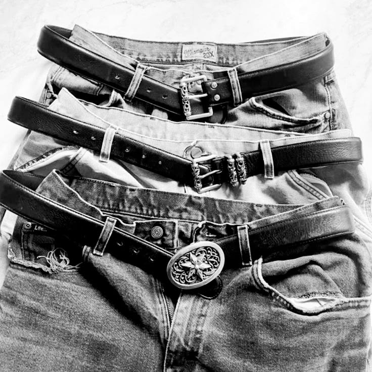 Three belts with different buckle styles laid over denim